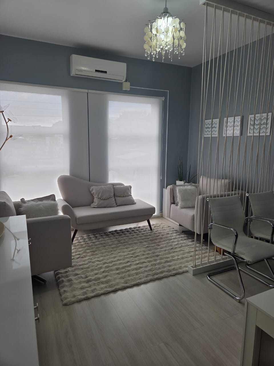 Sala de espera e atendimento com poltronas, tapete e lustre decorativo em tons neutros